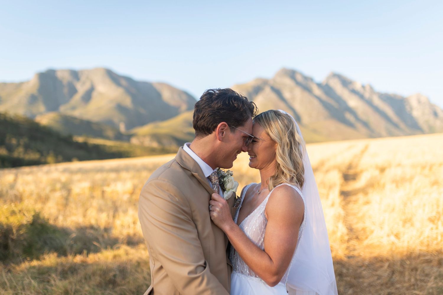 Bride and groom share a romantic moment in a golden field with stunning mountain backdrop on their wedding day.