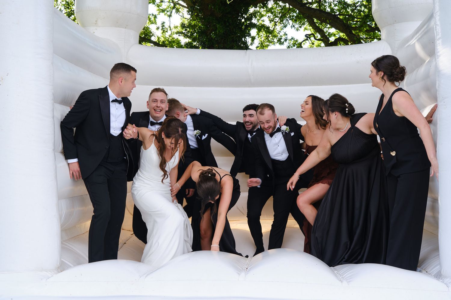 Elegant wedding reception hall with white round tables, black sashes, floral centerpieces, and fairy lights in a bright venue.