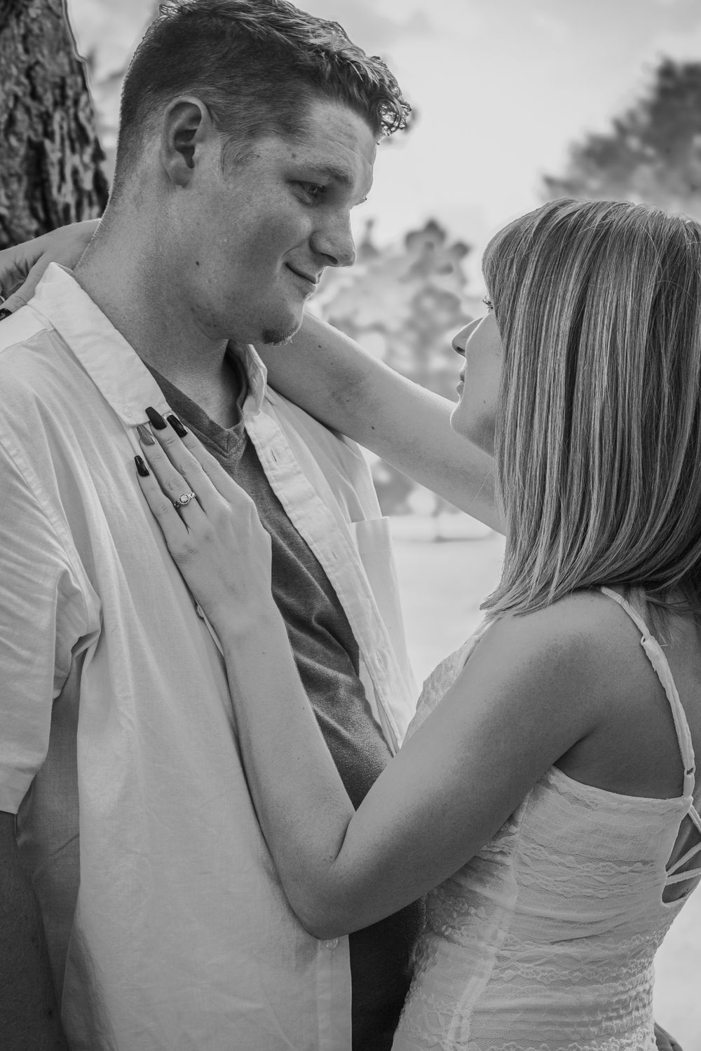 Black and white photo of a romantic couple sharing a tender moment outdoors, woman touching mans face affectionately.