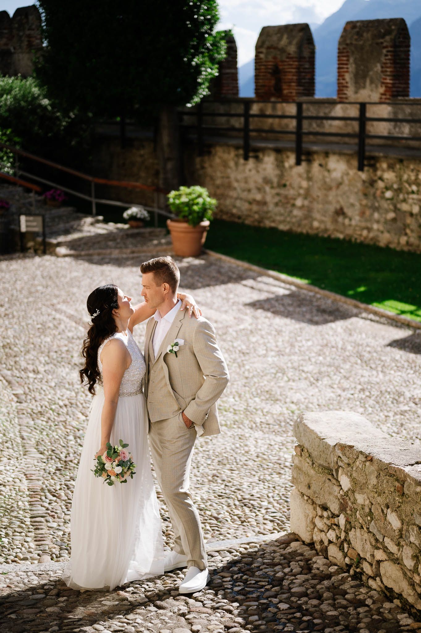 Bride and groom share a romantic moment on cobblestone courtyard of a historic Italian castle.