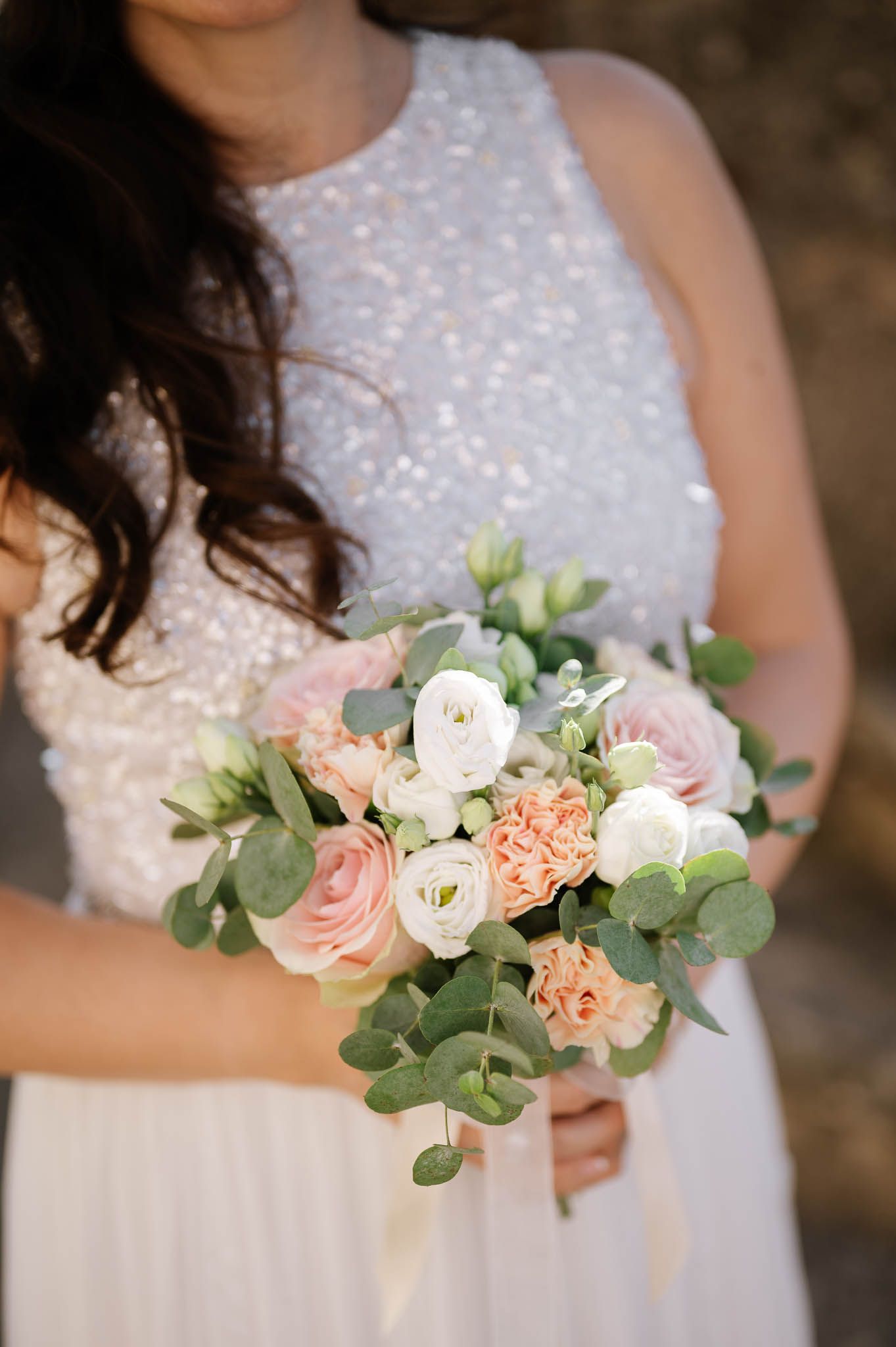 Bride holding a romantic bouquet of pink, peach, and white roses with eucalyptus greenery.
