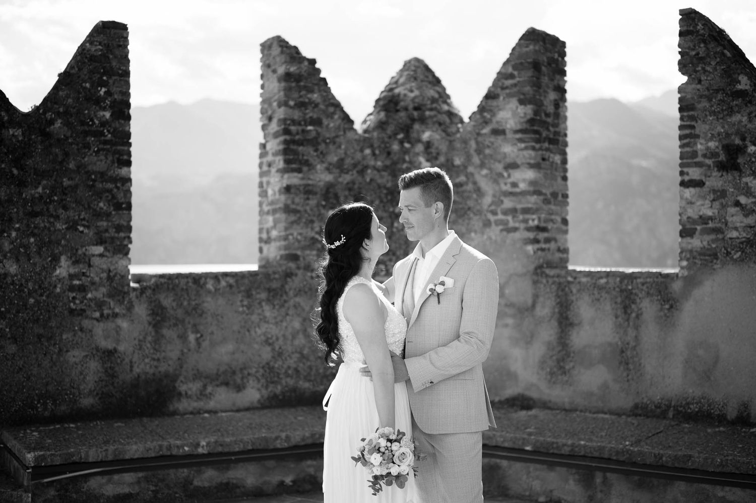 Black and white portrait of bride and groom embracing at historic castle battlements.