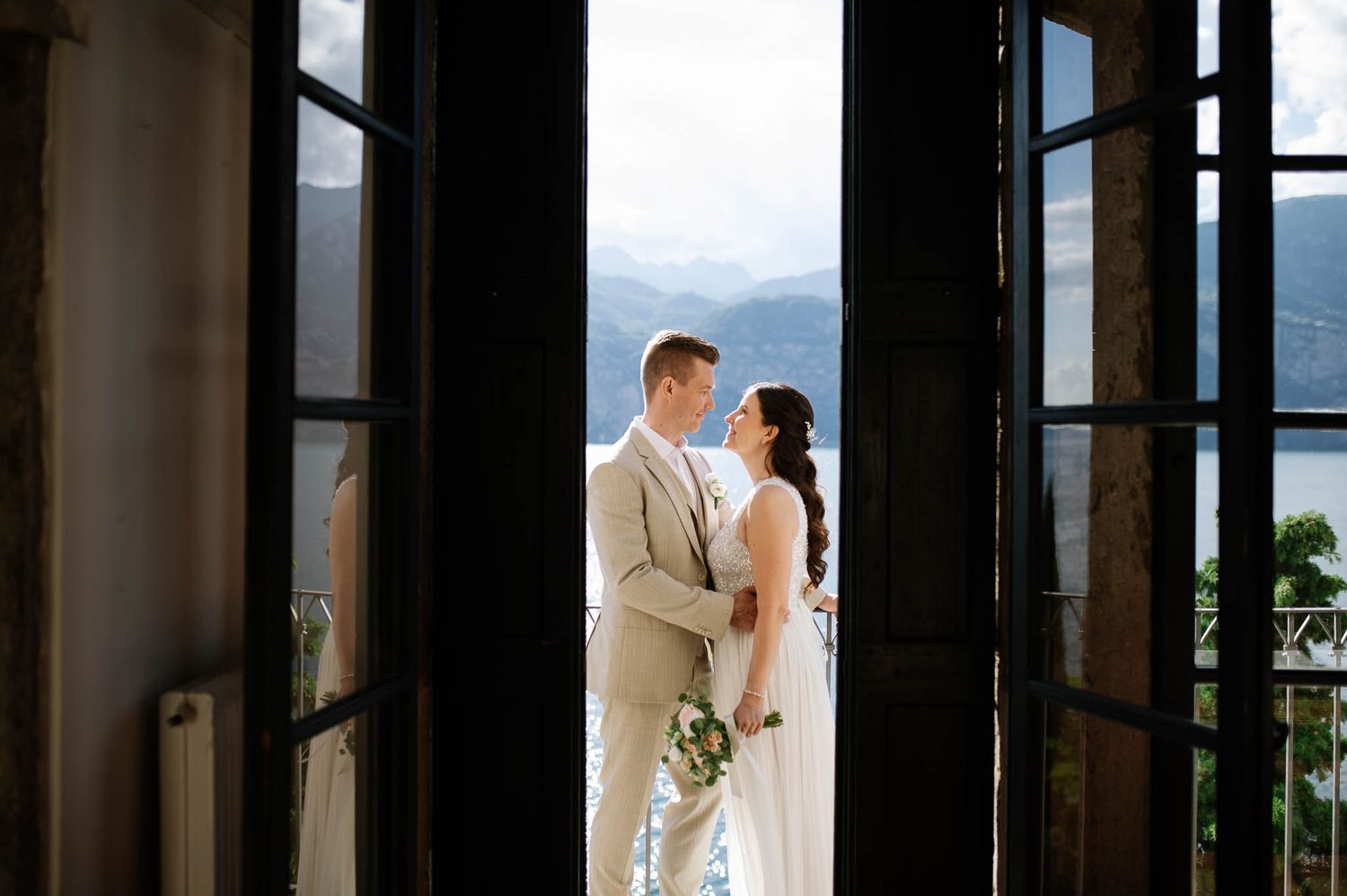 Romantic bride and groom embracing in elegant doorway with stunning lake and mountain views behind them.