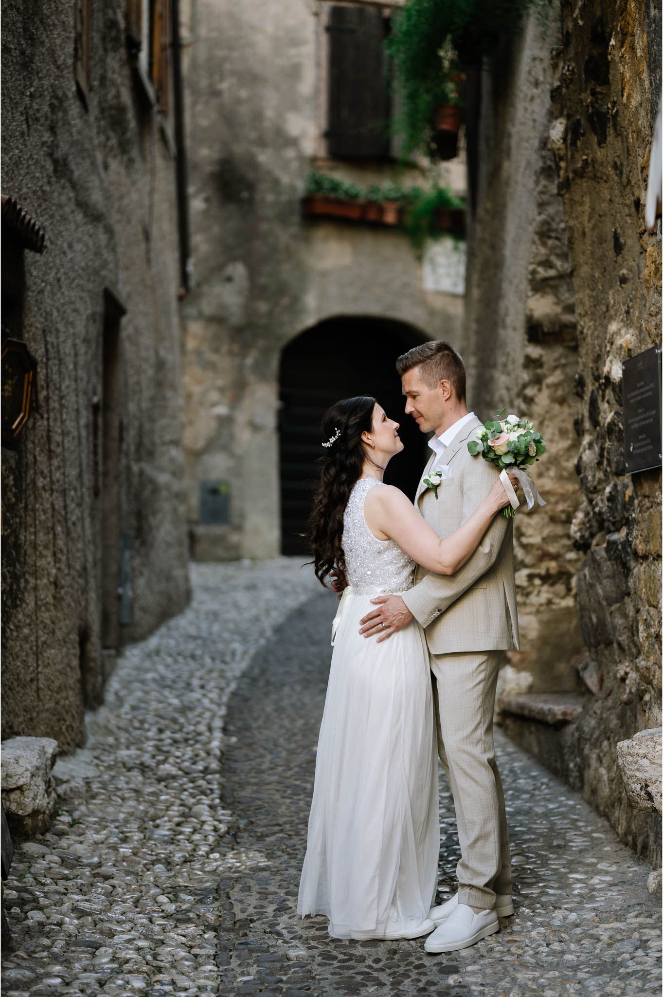 Bride and groom sharing romantic embrace in narrow cobblestone alley of picturesque Italian medieval village.
