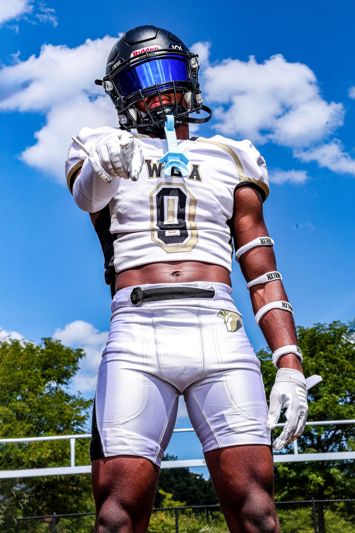 Football player in WGA #0 white and navy uniform with blue visor helmet pointing forward under blue sky.