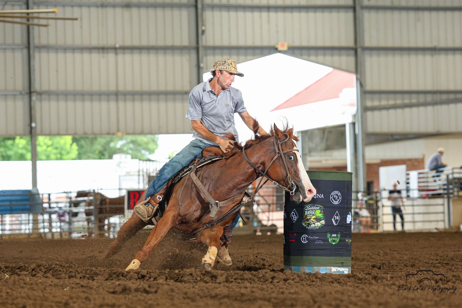 Barrel racer on chestnut horse rounding a barrel in an indoor rodeo arena during a competition.