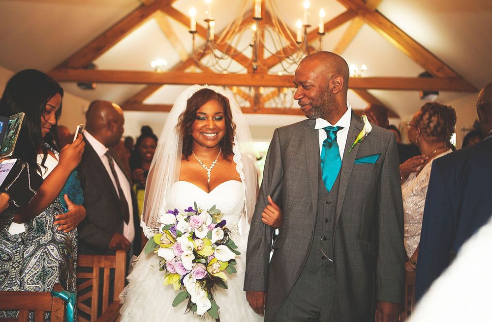 Bride and groom walk down the aisle in a rustic chapel, bride holding a white and yellow bouquet. At Oaks farm wedding venue in Surrey.