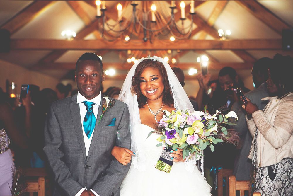 A joyful bride and groom walk down the aisle in a warmly lit wedding venue, bride holding a colourful bouquet. At Oaks farm wedding venue.
