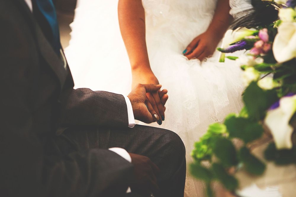 Bride and groom holding hands tenderly during wedding ceremony with floral bouquet nearby. At Oaks farm wedding venue in Surrey.
