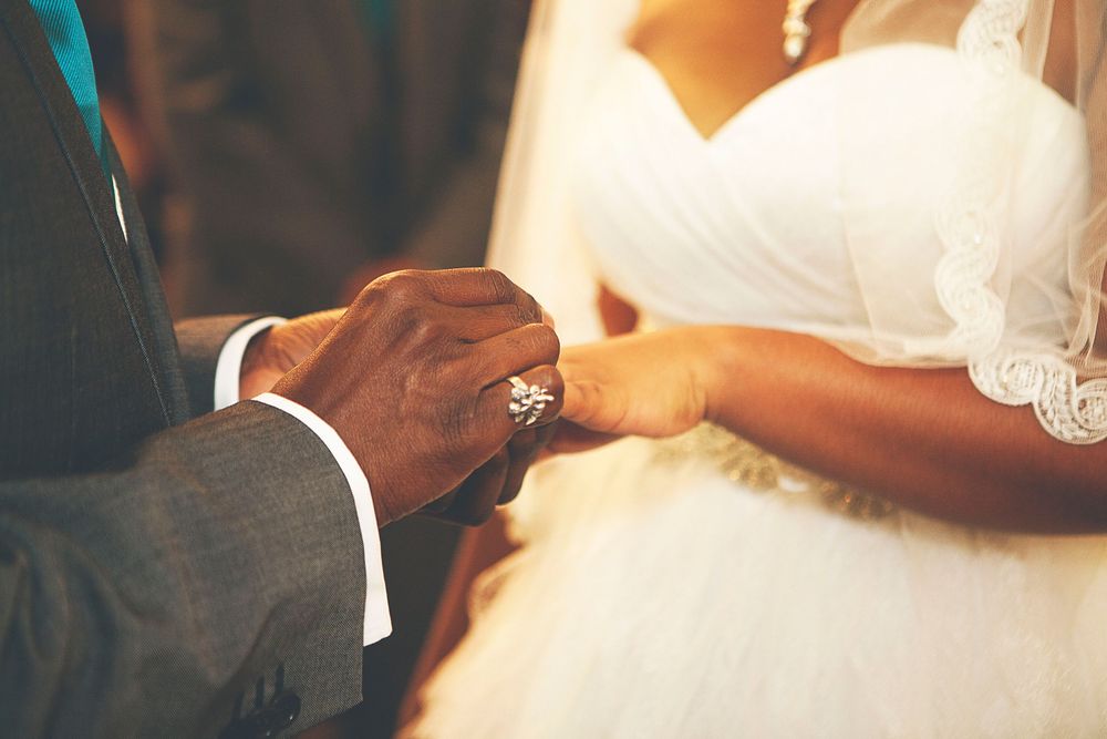 Groom placing a diamond ring on bride's finger during wedding ceremony, couple dressed in formal attire. At Oaks farm wedding venue.