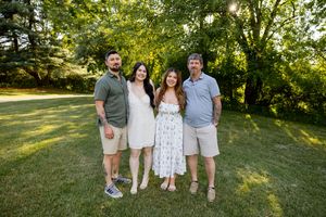 Family of four adults smiling together outdoors in a sunny green backyard during a casual family portrait.