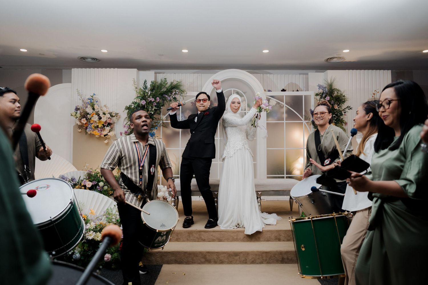 Muslim couple stands at wedding altar adorned with colorful floral arrangements in elegant indoor ceremony venue.
