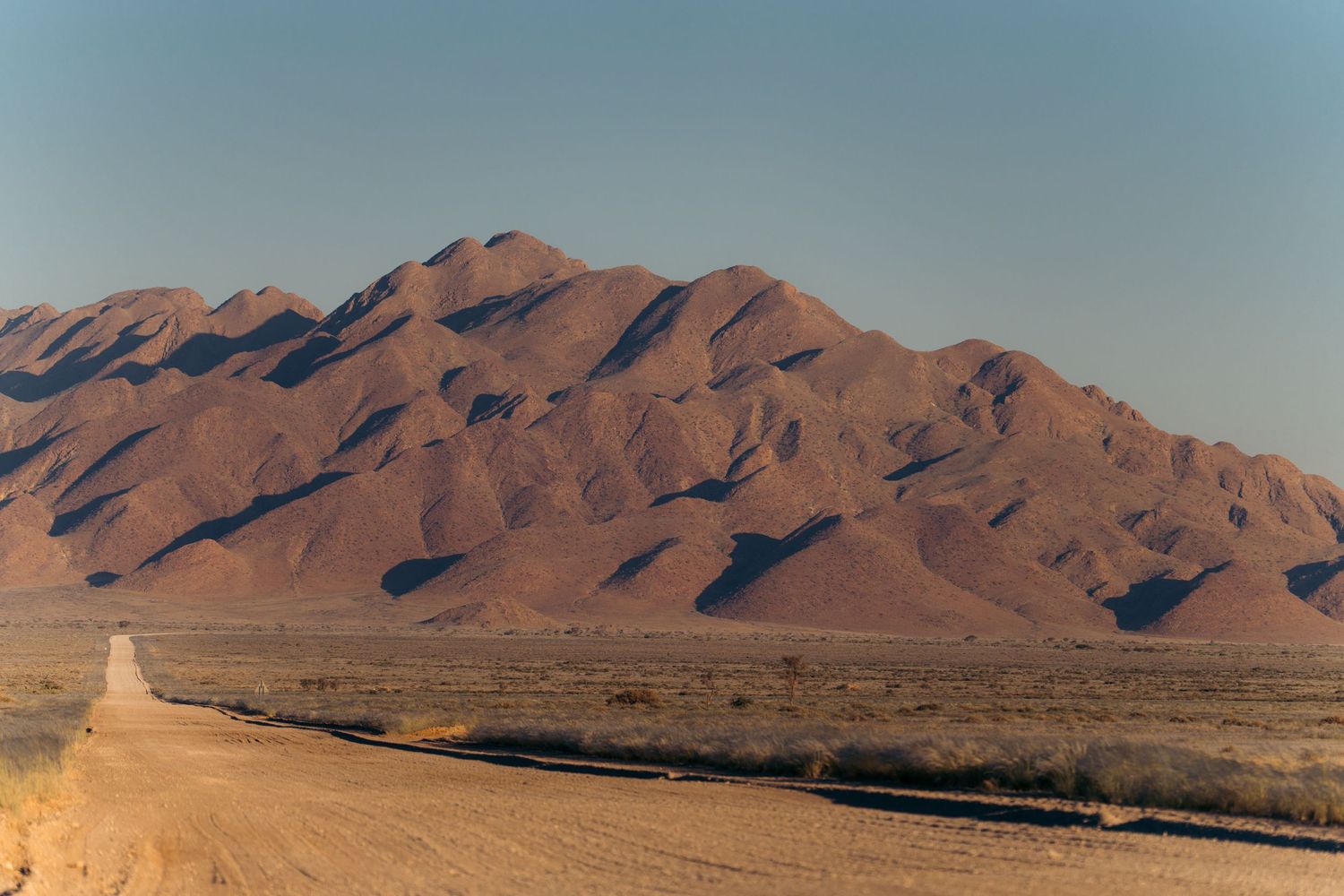 montagnes vallonnées rouges devant une piste de sable en namibie