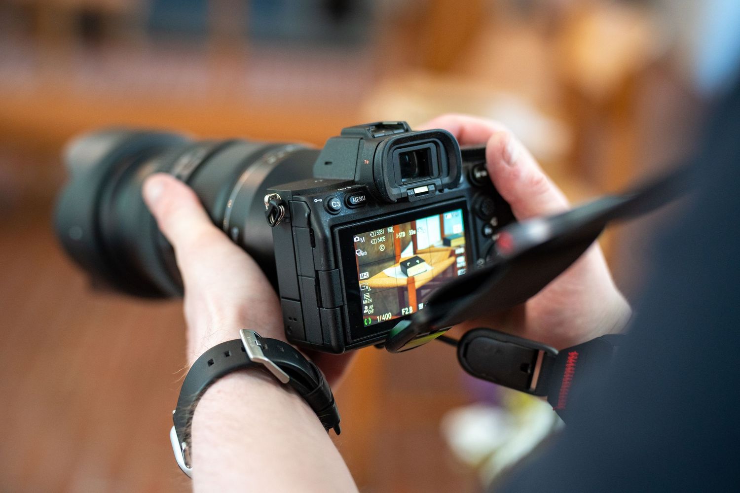 Person holding a DSLR camera with a zoom lens, reviewing photos on the LCD screen.