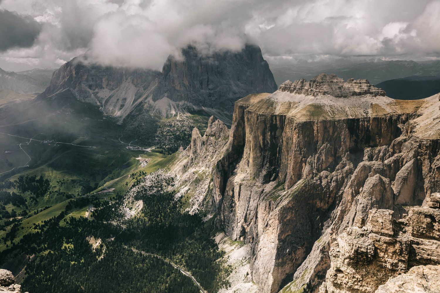 Dramatic Dolomite mountains with jagged rocky peaks, winding road, and moody overcast sky in the Italian Alps.