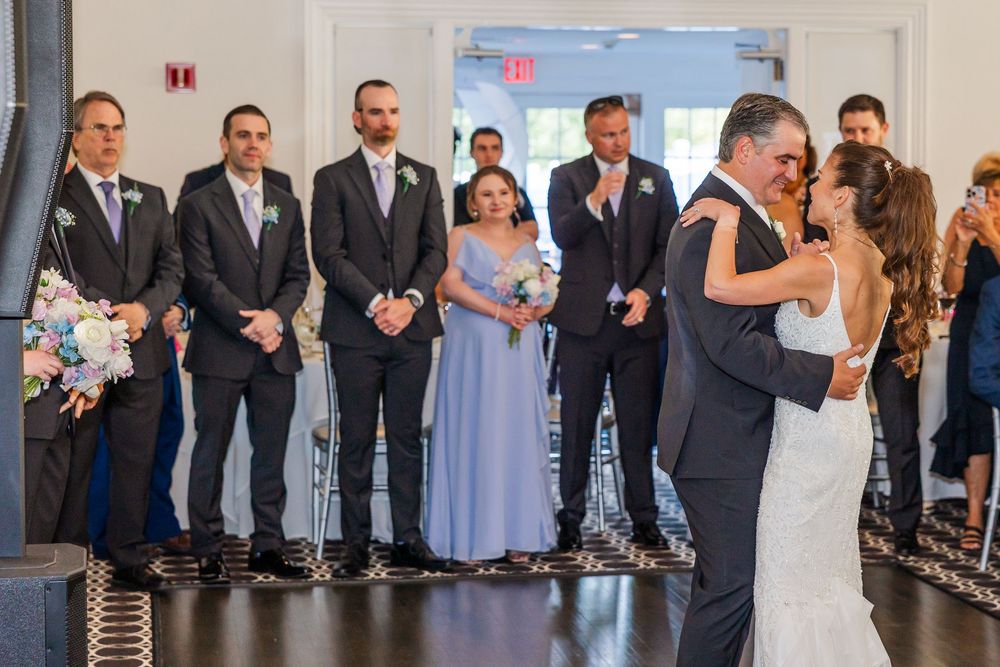 Bride and groom share their first dance while groomsmen and guests watch during an elegant indoor wedding reception.
