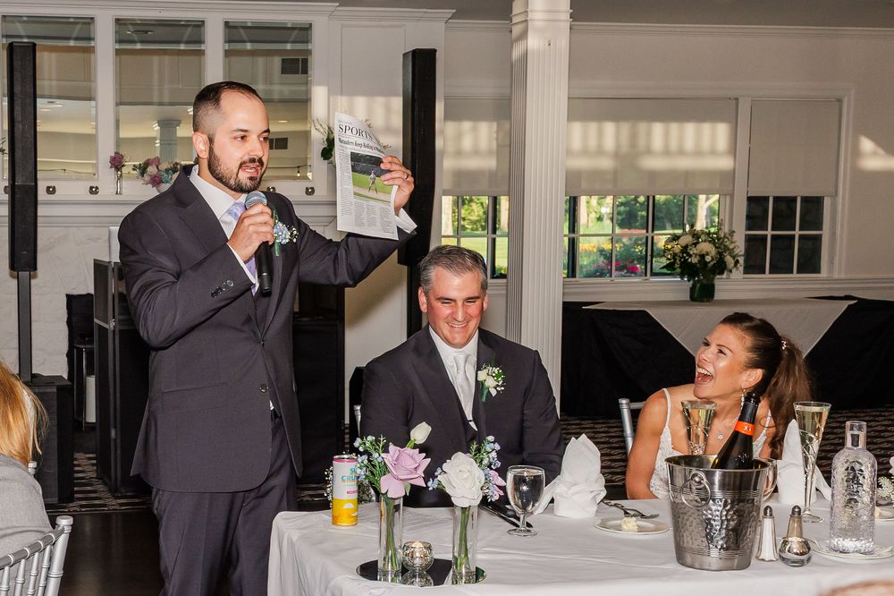 Man giving a toast speech at a wedding reception while the groom and bride sit at the head table.