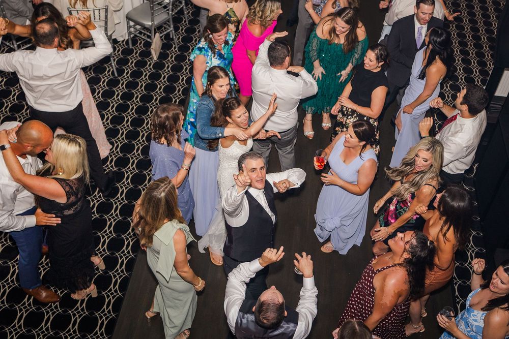Guests dancing and celebrating on a crowded wedding reception dance floor in a elegant ballroom venue.
