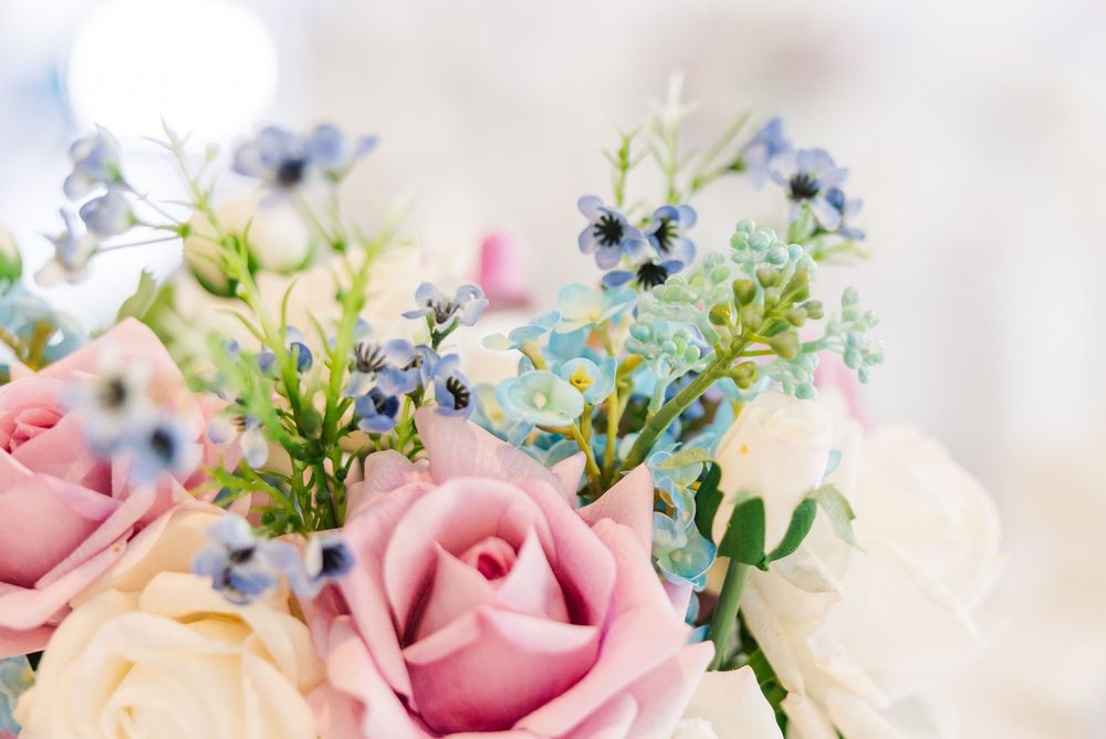 A beautiful wedding bouquet featuring soft pink roses, white flowers, and delicate blue blooms with green foliage.