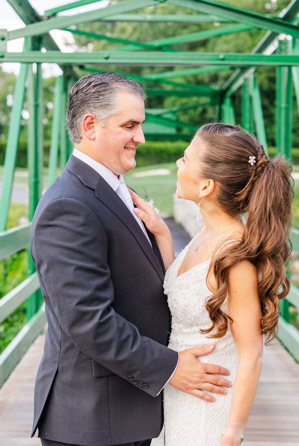 Bride and groom share a romantic moment on a green bridge surrounded by lush greenery.