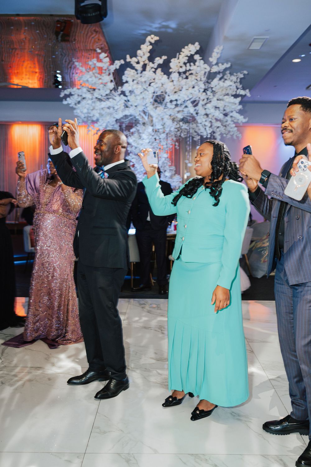 Guests celebrating at an elegant event, dancing joyfully near a white floral tree centerpiece in a stylish venue.