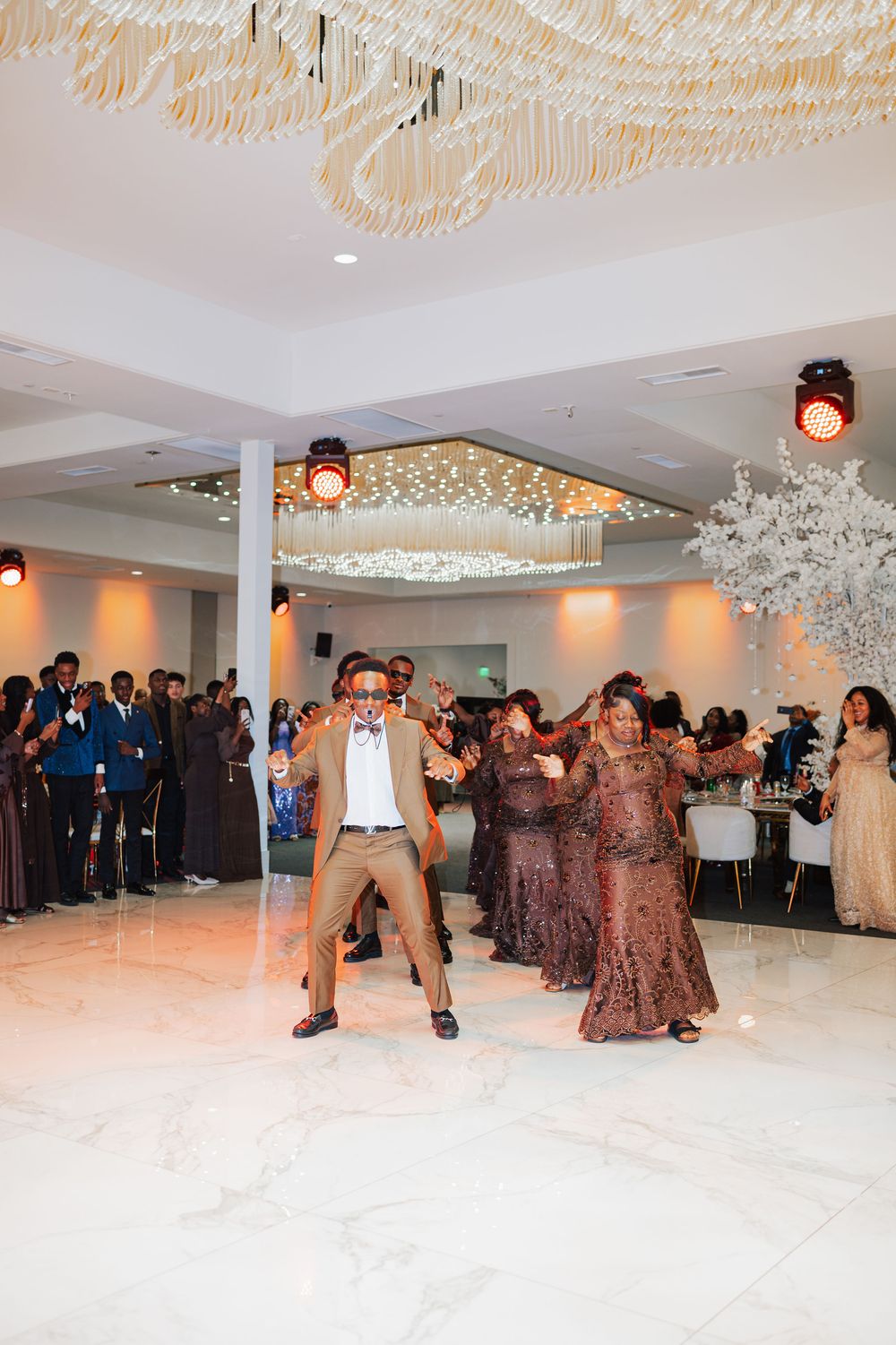 Wedding guest performs energetic dance moves on white marble floor at lively reception celebration.