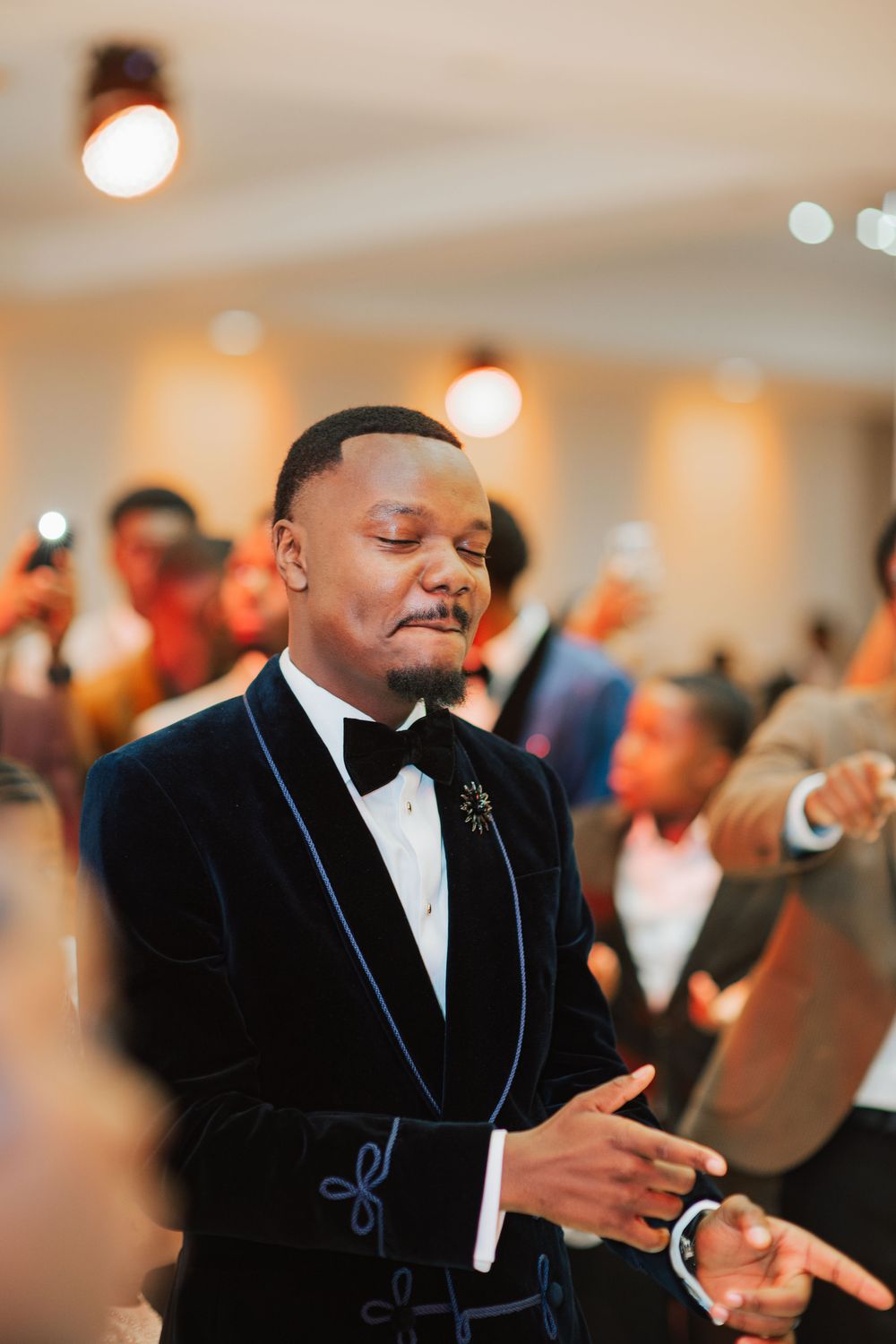 Stylish man in navy velvet tuxedo with bow tie smiling at elegant indoor event celebration.
