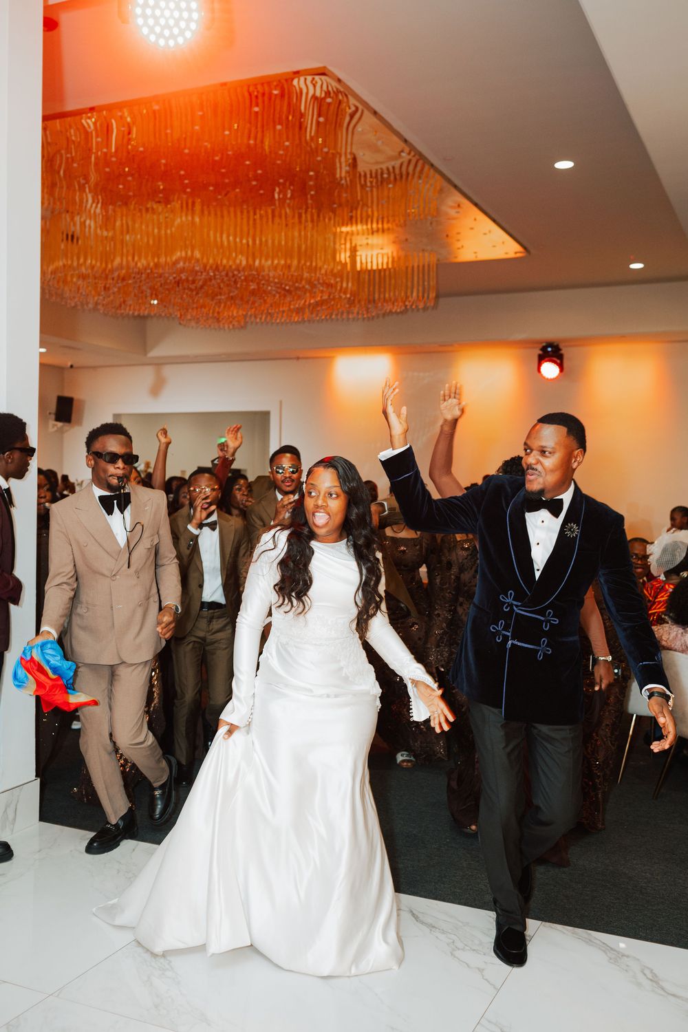 Bride in white gown and groom in navy tuxedo make grand entrance at elegant wedding reception.