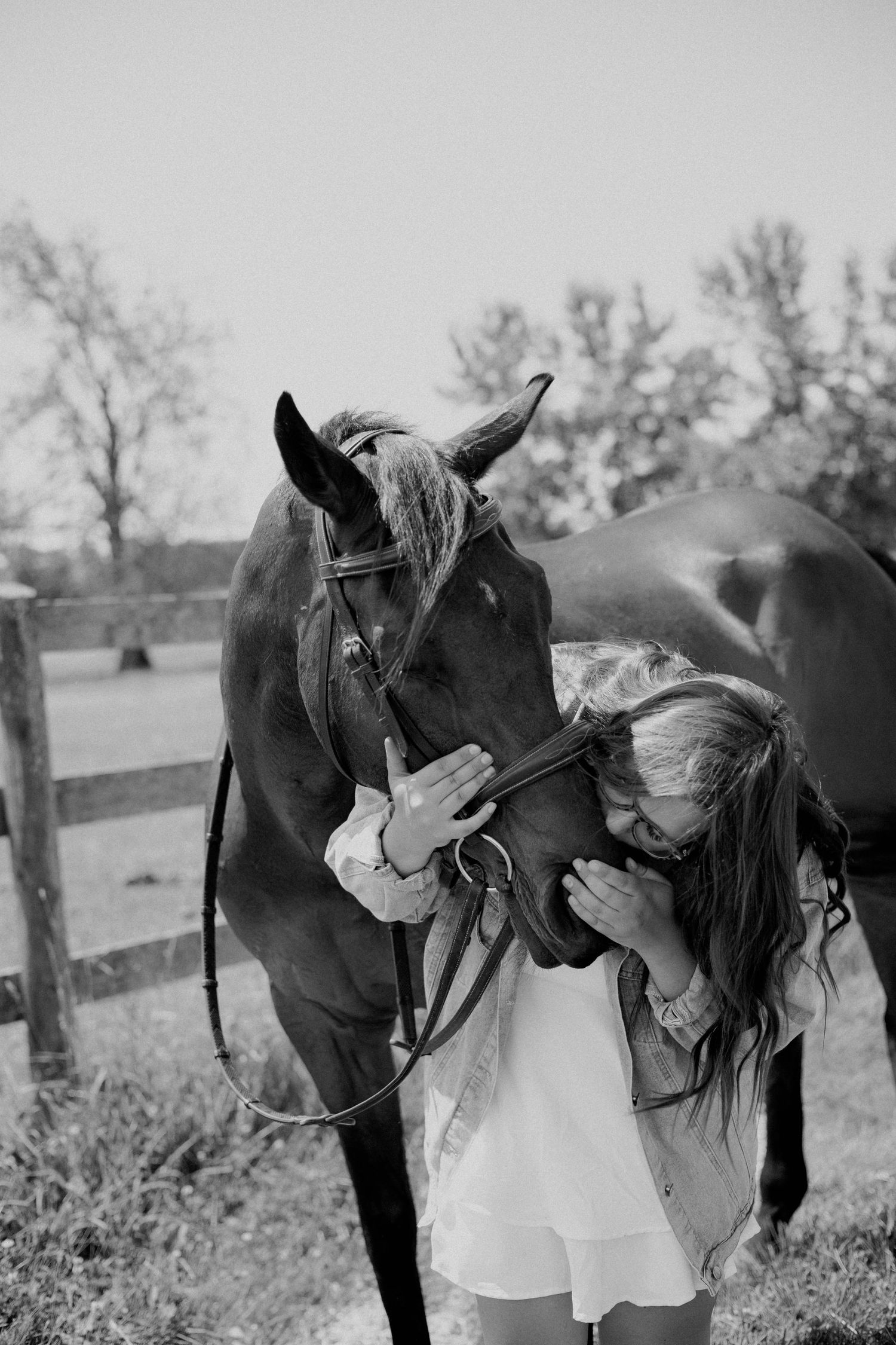 Girl in white dress kissing a bay horse on the nose in a black and white farm photo.