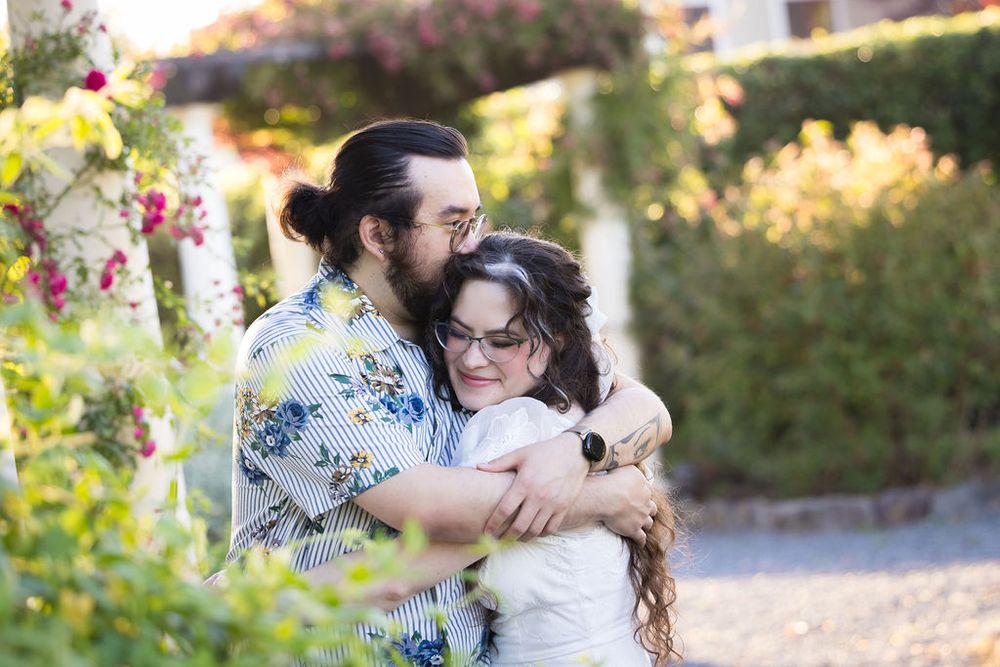 Couple embracing warmly in a sunny garden surrounded by colorful flowers and greenery.