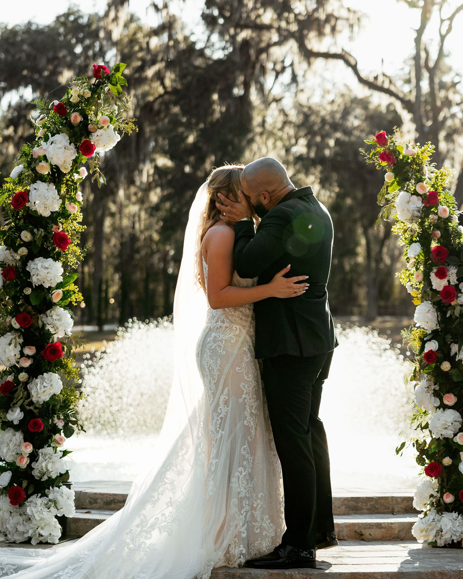 Bride and groom share a romantic moment on a white Victorian porch surrounded by lush greenery.
