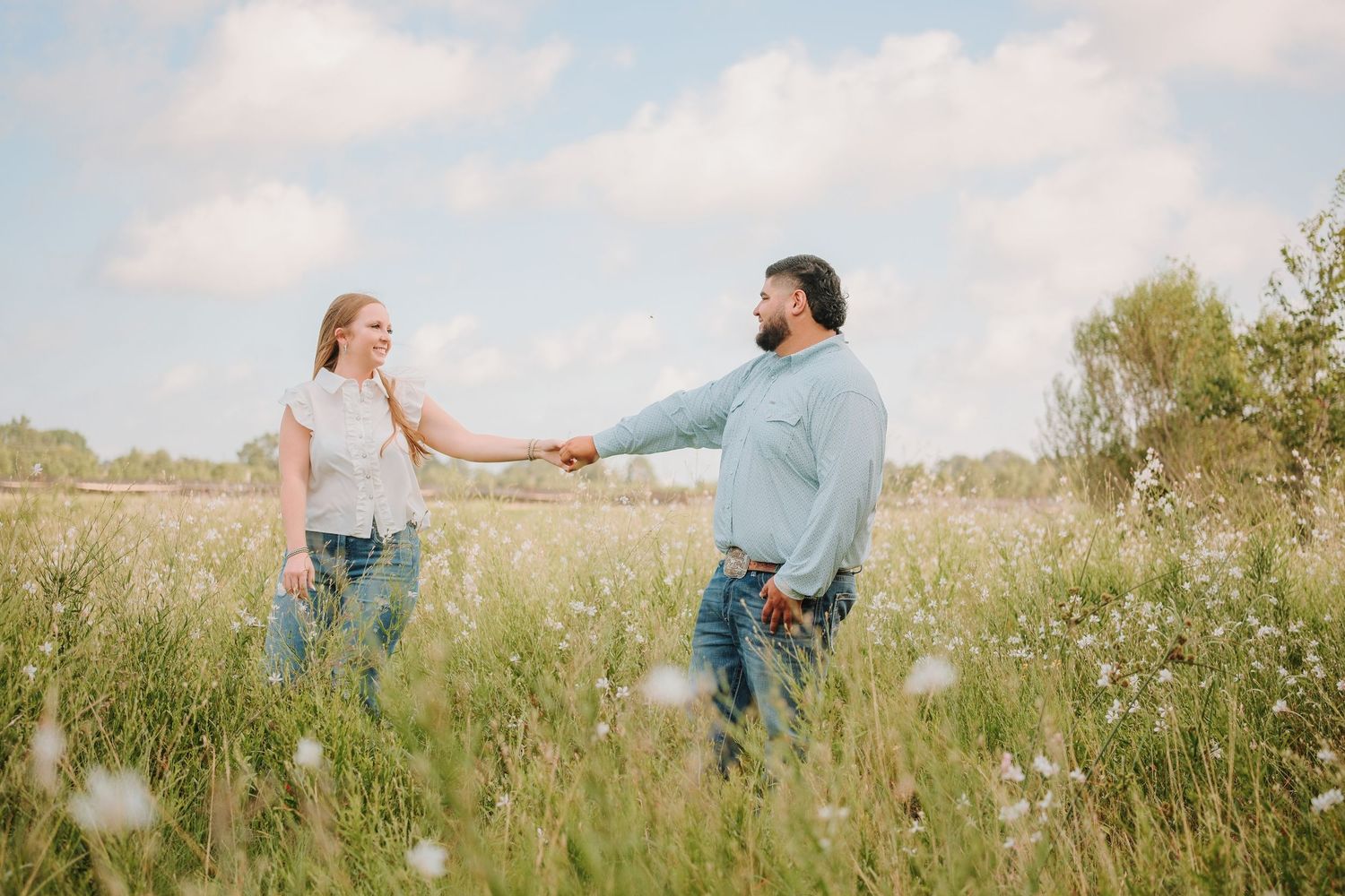 Couple holding hands walking through a wildflower meadow under a cloudy sky.