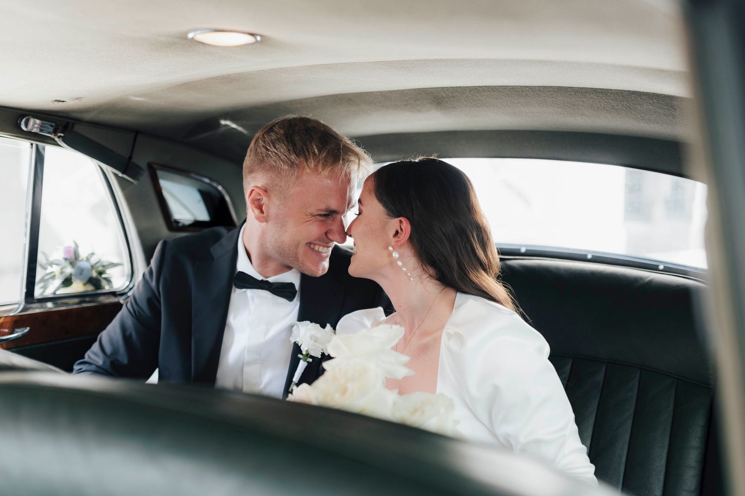 Bride and groom sharing a romantic moment in a classic car on their wedding day.