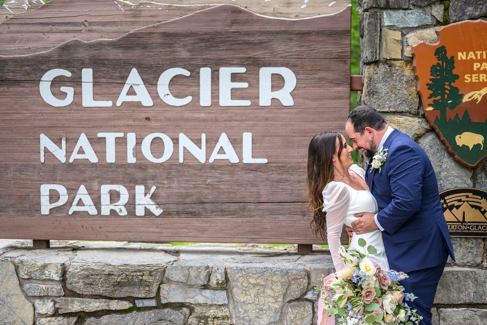 Couple sharing a kiss in front of the Glacier National Park entrance sign on their wedding day.