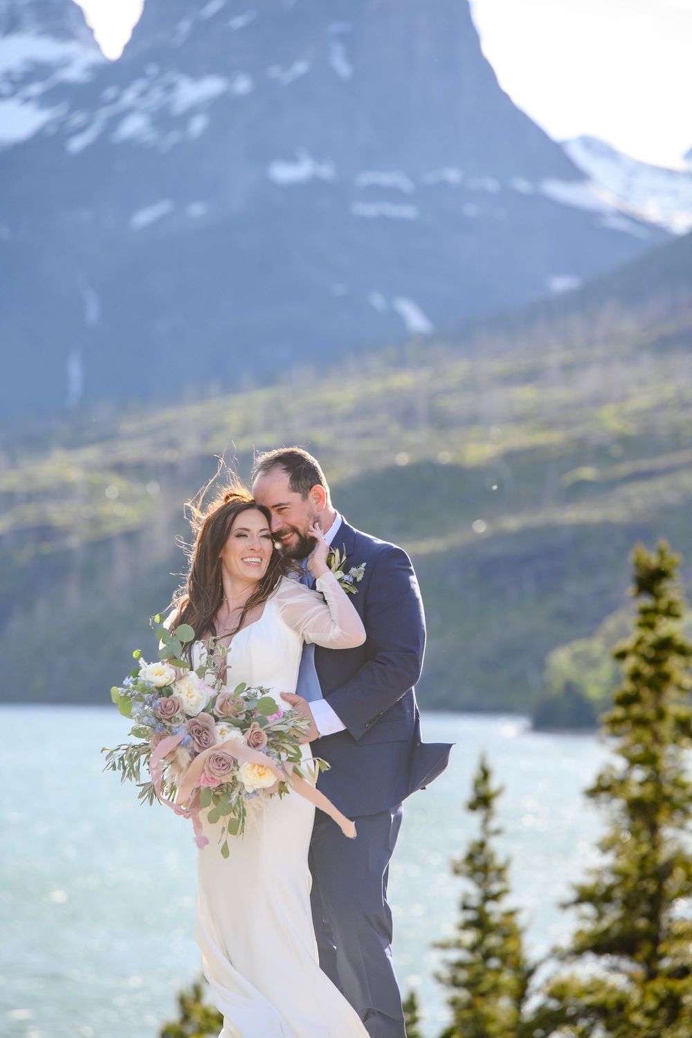 Bride and groom embrace with mountain lake backdrop at Glacier National Park wedding elopement.