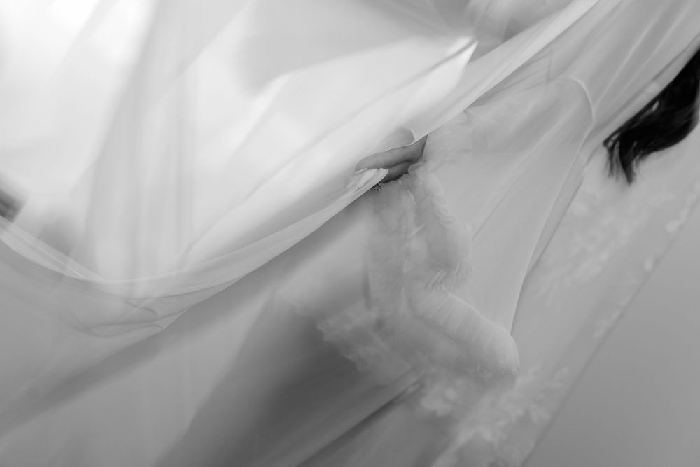 Artistic black and white photo of bride wrapped in flowing sheer wedding veil fabric.