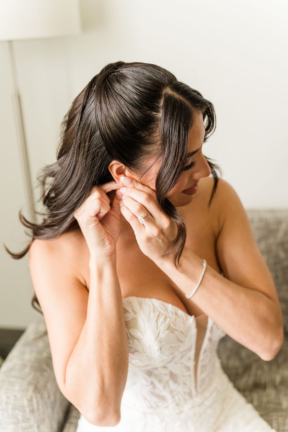 Bride in strapless lace gown putting on earring while getting ready for her wedding day.