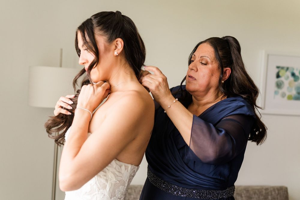 Mother helping bride fasten her wedding dress in a hotel room before the ceremony.