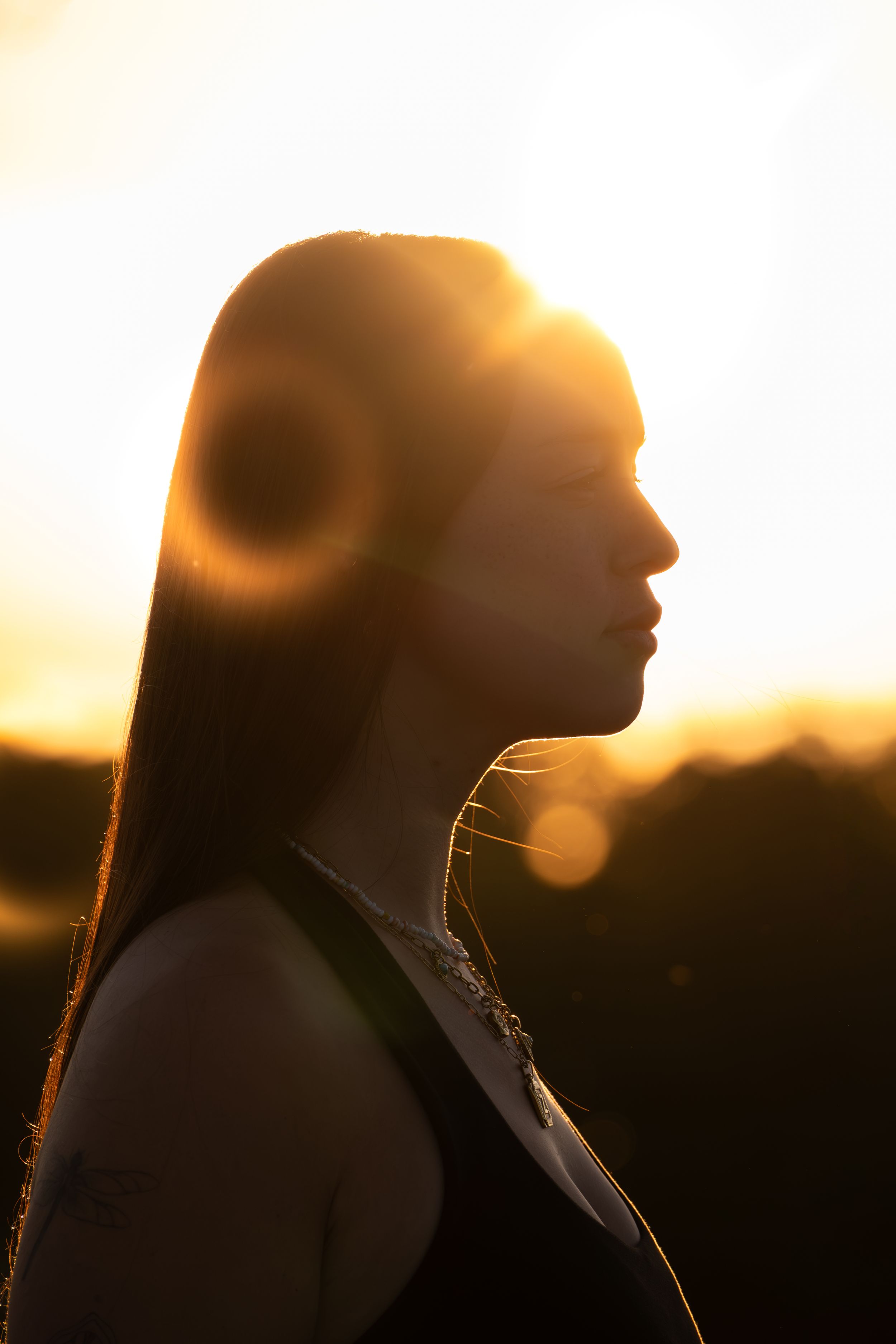 Silhouette of a young woman with long hair wearing headphones against a golden sunset backlight.