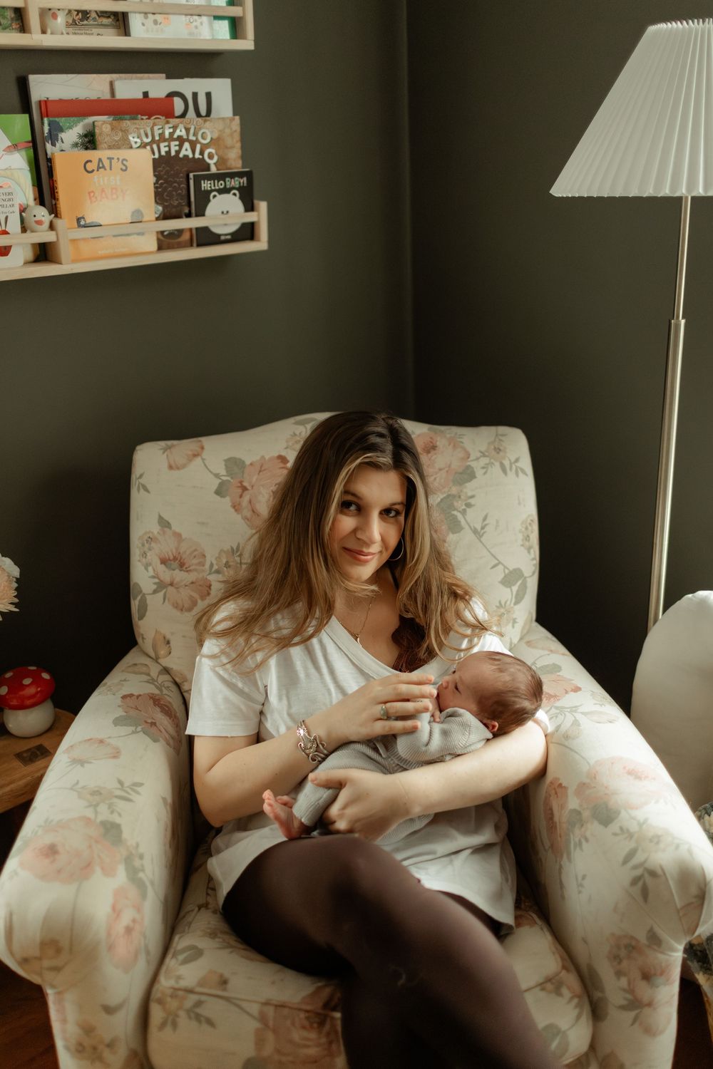 New mother sitting in floral armchair bottle feeding her newborn baby in a nursery.