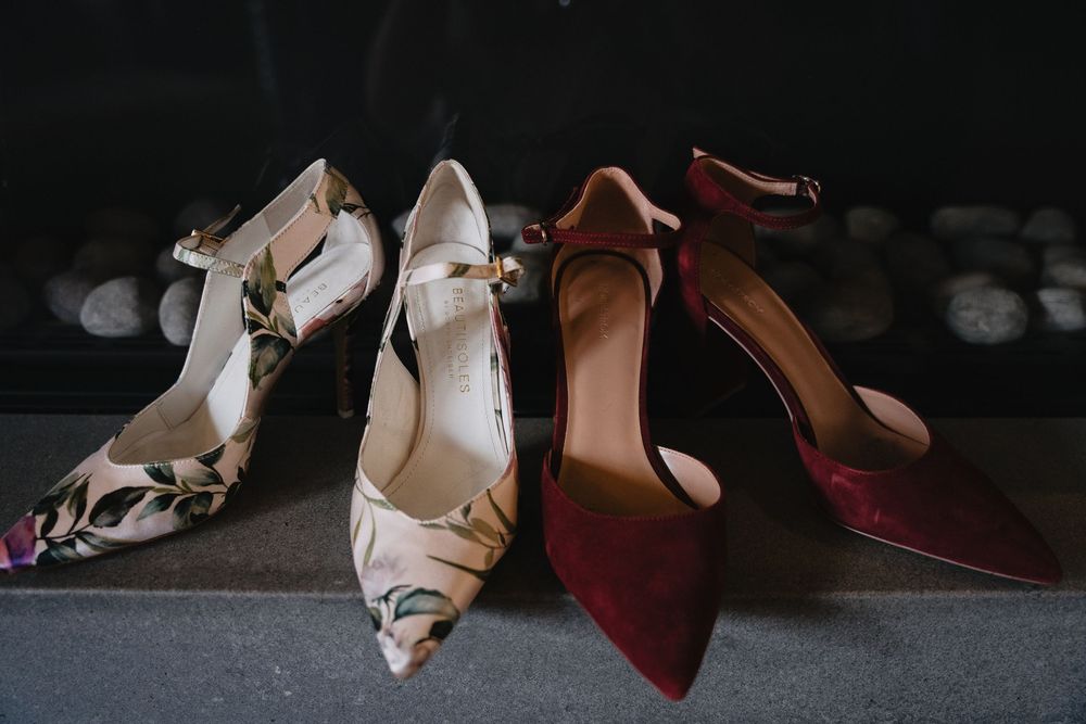 Two pairs of elegant heels, floral and burgundy velvet, displayed on a dark surface for a wedding.