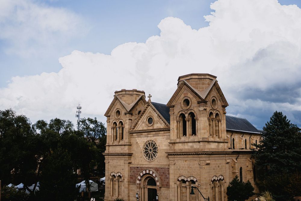 Historic Cathedral Basilica of Saint Francis of Assisi in Santa Fe, New Mexico, under dramatic cloudy skies.