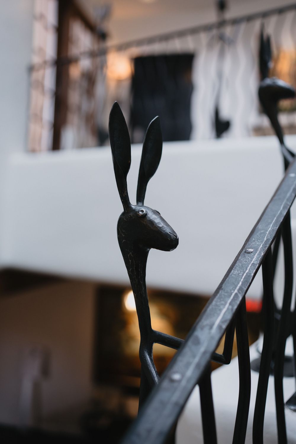 Black metal rabbit sculpture decorating a staircase railing in a modern interior space.