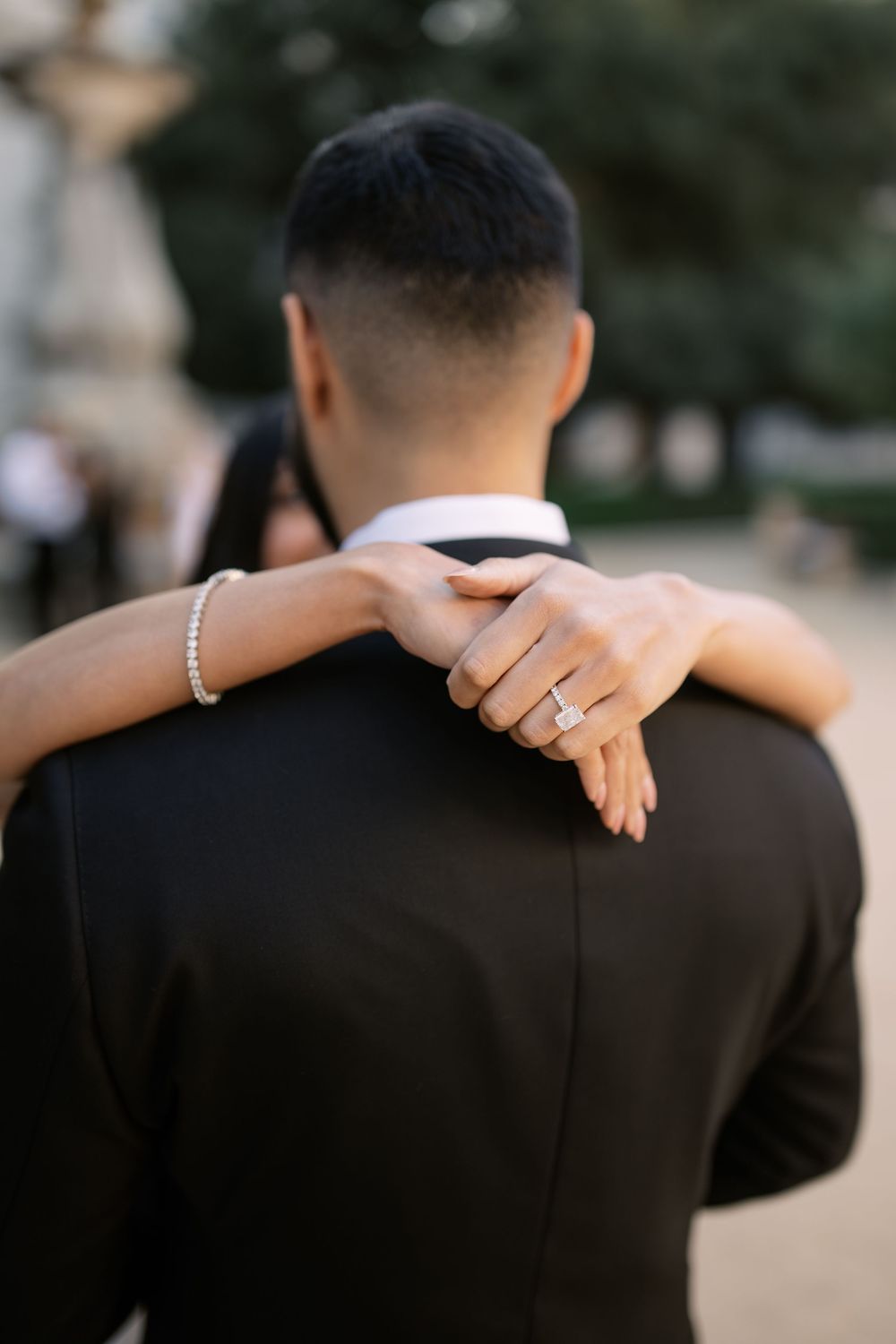 Bride rests hand on groom's shoulder showcasing diamond engagement ring and bracelet during wedding photo session.