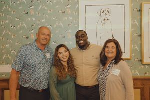 Four people smiling together in a room with dog-themed wallpaper and framed dog artwork.