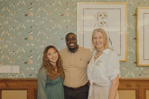 Three people posing together smiling in front of decorative dog-themed wallpaper and framed art.