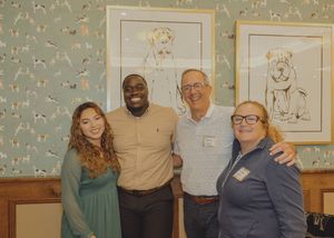 Four people smiling together in front of dog-themed wallpaper art at an indoor event.