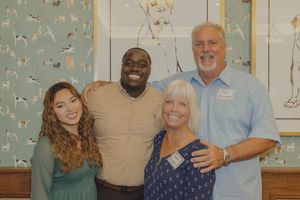 Four smiling people pose together indoors in front of a decorative wall with animal artwork.