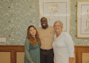 Three people smile together in front of dog-themed wallpaper at a social event.