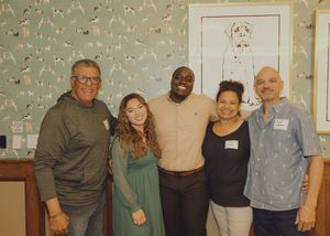 Five people smile together in front of dog artwork at an indoor event.